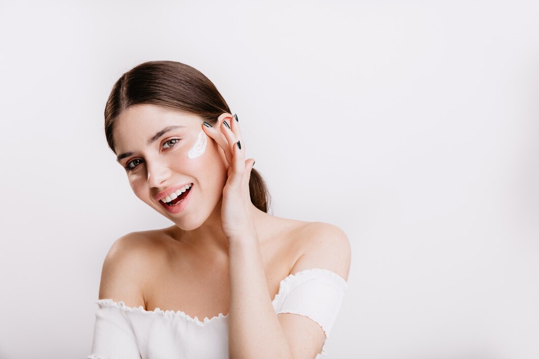 smiling-green-eyed-girl-puts-cream-clean-face-brunette-white-top-posing-isolated